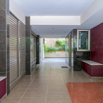 perspective photograph showcasing the leading lines of a tiled entrance hallway, dark granite paneling, and a sunlit courtyard backdrop.