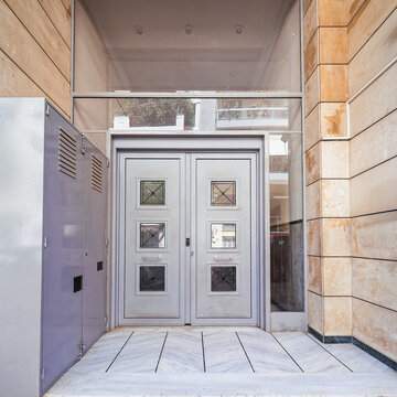 Front view of a classic 1970s Athenian residential building entrance with grey double doors and marble flooring in Athens, Greece.