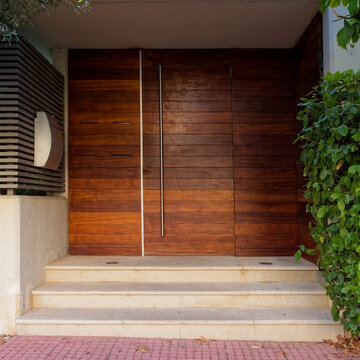 Symmetrical architectural shot framing the rich wood grain textures, stainless steel pull bar, marble steps, and metal louver details.