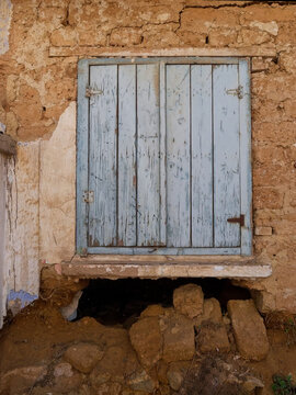 Atmospheric stock photograph of a rustic, abandoned house window with blue wooden shutters, ideal for editorial, travel, and historic preservation media.
