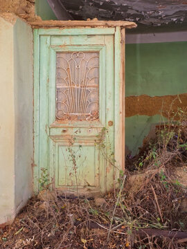 Detailed vertical photo of a vintage mint-green wooden door with art deco ironwork in an abandoned Athenian building, Athens, Greece.
