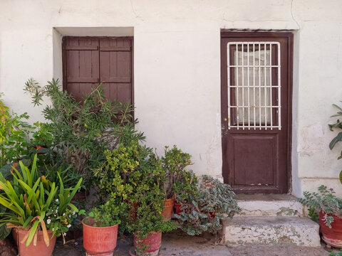 Front view of a humble traditional Greek house facade with dark wooden door, window shutters, and potted plants in Athens, Greece.