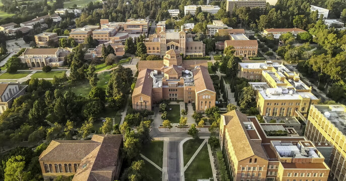 Aerial view of the UCLA campus featuring historic red-brick buildings with terracotta roofs, lush green trees, and manicured lawns in Westwood, California, United States.
