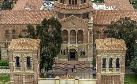 Aerial view of Royce Hall at the UCLA Campus with its red brick facade, terracotta roof, and students walking on the plaza below in Westwood, California, United States.
