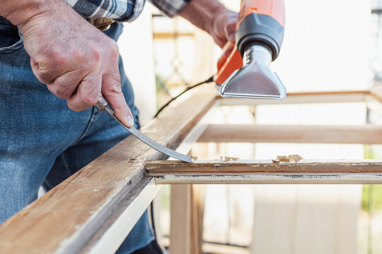 Carpenter using heat gun and wood scraper removes paint from old wooden window. Construction industry, carpentry. Restoration. 