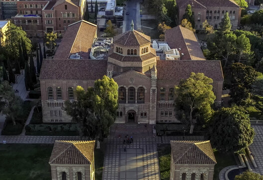 Aerial view of Royce Hall at UCLA Campus, featuring Romanesque Revival architecture, red-tiled roofs, and surrounding trees in golden hour light in Westwood, California, United States.