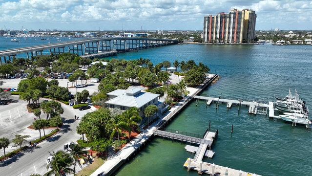 Aerial view of the Hillsboro Inlet Bridge and marina with a high-rise residential building, lush palm trees, and boats docked in the clear coastal waters in Pompano Beach, Florida, USA.