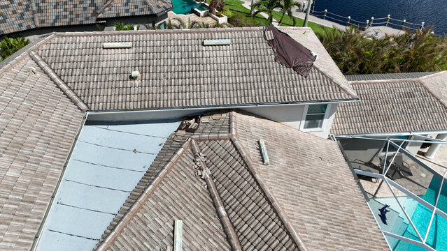 Aerial view of damaged residential roof with missing tiles and a protective tarp, Florida, USA.