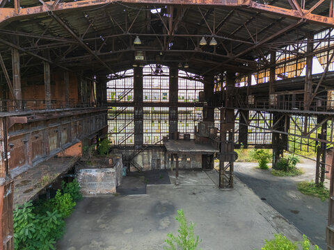 Aerial view of an abandoned metallurgical plant interior with rusted steel trusses, factory platforms and vegetation reclaiming the closed industrial complex in Ozd, Hungary.