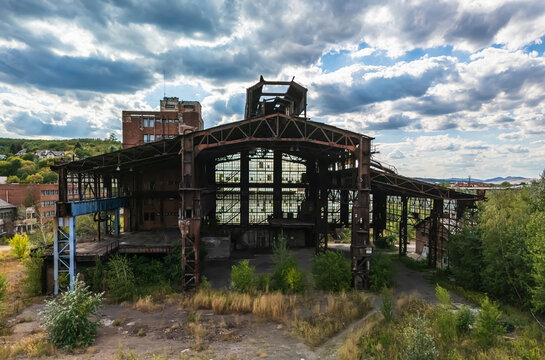 Aerial view of an abandoned structure at the former metallurgical plant in Ozd, Hungary, with rusted steel girders, broken windows, and summer vegetation reclaiming the industrial site.