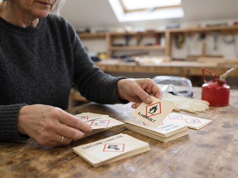 Woman sorting flammable hazard cards during a safety training exercise in a workshop with protective equipment nearby.