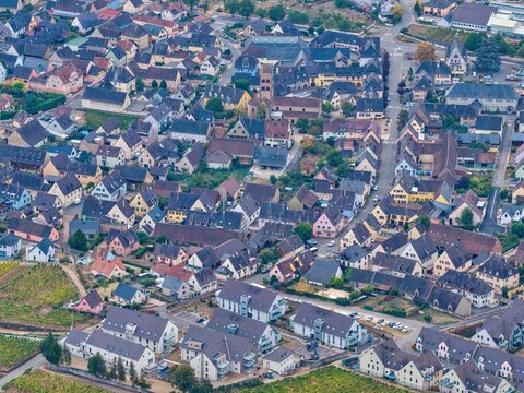 Aerial view of the historic town of Colmar featuring traditional half-timbered houses, a prominent church tower, narrow streets, and surrounding vineyards in Colmar, Grand Est, France.