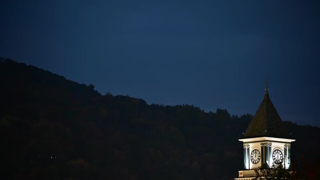 Time lapse transition from early dark morning in to morning overcast day clouds, Clock tower architecture in the foreground, Bradford Pennsylvania USA valley town 4K resolution video clip