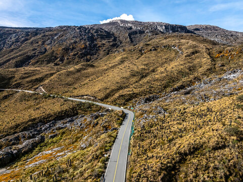 Aerial view of the winding road leading towards the Nevado del Ruiz volcano, surrounded by rugged Andean paramo landscape with rocky slopes in Villamaria, Caldas, Colombia.