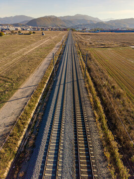 Aerial view of railway tracks stretching through open fields towards the city of Brasov with mountains in the background, Brasov, Brasov, Romania.