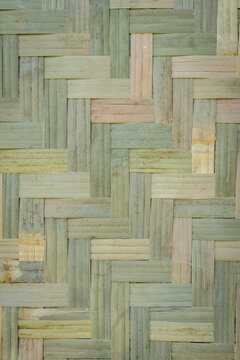 Interwoven bamboo strips arranged in a repeating geometric pattern, displaying natural beige, tan, and muted green tones with visible fibers and textured surfaces.