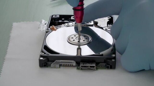 Hand in gloves carefully handles open hard drive. Disk spins slowly during repair. Focus on mechanical parts and precision. Suitable for tech tutorials, data recovery, or engineering projects