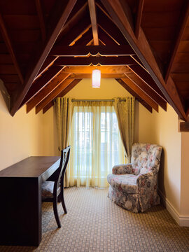 cozy attic room with wooden vaulted ceiling, dark wood desk and armchair by the window, interior architecture, warm cottage living concept with copy space