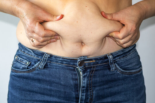 Woman pinching belly fat over jeans showing abdominal skin and body image concern