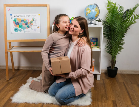 Mother giving a gift to her daughter in a cozy home setting, symbolizing support in learning and development. Warm family interaction, education, parenting care, and growth.