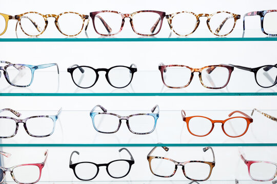 Eyeglass frames displayed on illuminated shelves in optical store offer prescription eyewear options for vision correction, fashionable accessories and retail shopping.