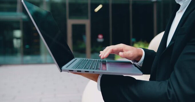 Close-up of businessman typing on a laptop outdoors, representing remote work, digital communication and modern technology.