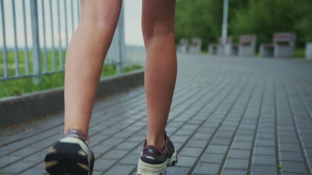 Runner moves steadily on paved path beside railing. Legs show effort, rhythm, and focus in slow motion. Shoes grip pavement with each step, suggesting fitness. Ideal for health, wellness