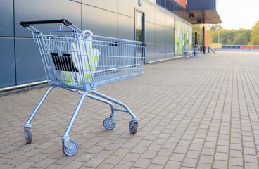 Metallic shopping cart filled with plastic grocery bag stands on paved parking lot outside supermarket against autumn backdrop © yaviki