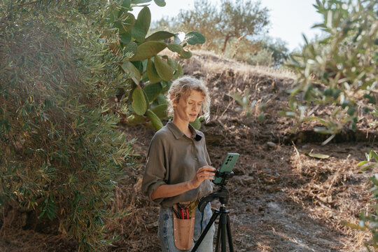 Female Gardener Adjusting Smartphone on Tripod for Video Recording Outdoors