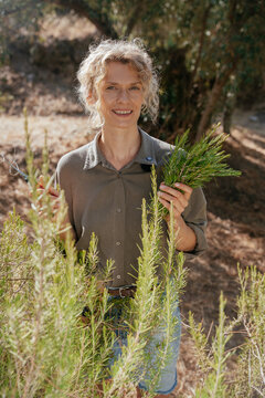 Smiling Woman Holding Fresh Rosemary Bouquet in Sunny Mediterranean Herb Garden