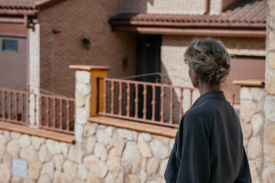 Blonde Woman Standing Outside Rustic Country House Viewed from Behind