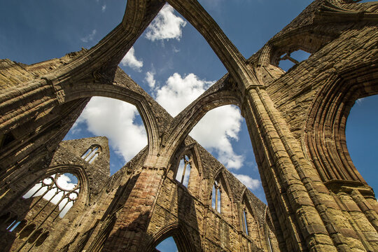 Architectural stone arches of Tintern Abbey ruins against a blue sky
