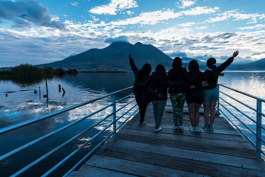 Group of young female friends enjoying the scenic view of San Pablo Lake and Imbabura Volcano from a wooden pier in Otavalo, Ecuador