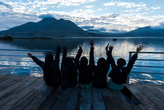 Group of young female friends enjoying the scenic view of San Pablo Lake and Imbabura Volcano from a wooden pier in Otavalo, Ecuador