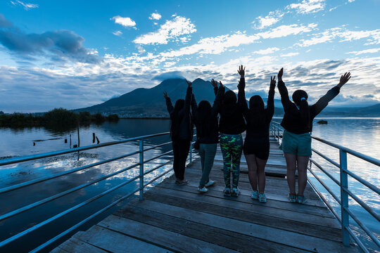 Group of young female friends enjoying the scenic view of San Pablo Lake and Imbabura Volcano from a wooden pier in Otavalo, Ecuador