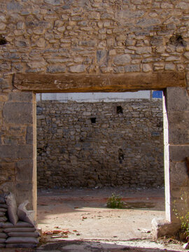 Antigua entrada sin puerta en una r&uacute;stica muralla de piedra, con dintel de madera, que revela un patio interior abandonado y sacos de arena.