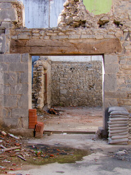 Antigua entrada sin puerta en una r&uacute;stica muralla de piedra, con dintel de madera, que revela un patio interior abandonado y sacos de arena.