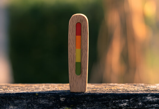 A wooden risk indicator featuring a vibrant red, orange, yellow, and green scale on a rustic outdoor ledge, conveying measures, warnings, performance, evaluations, and monitoring.