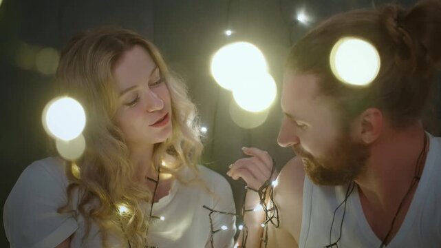 Warm lights glow softly around two embracing lovers. Their faces beam with affection as they lean close. The gentle glow adds romantic warmth to the moment. Ideal for intimate, cozy