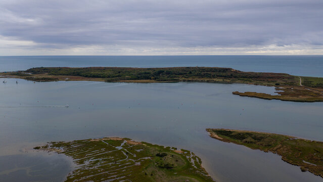 Aerial view of Stanpit Marsh featuring marshland, tidal waters, and a distant coastline under a cloudy sky in England, United Kingdom.