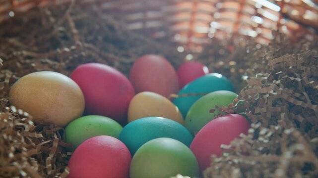 Colorful eggs nestle in soft brown bedding. Woven basket frames the cozy, festive scene. Warm light highlights each egg's hue and texture. Springtime tradition captured in quiet stillness