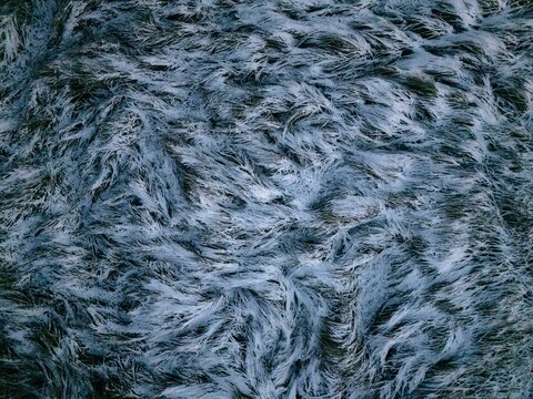 Aerial view of frost-covered grass blades creating a textured pattern across the frozen landscape in Uusimaa, Finland.