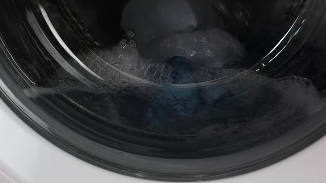 In a washing machine, a drum with water and detergent is spinning. Medium shot.