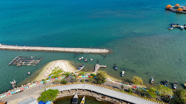 Aerial view of Jepara Kartini Ferry Terminal with boats docked along the coast, a breakwater, and calm turquoise waters in Jepara, Central Java, Indonesia.