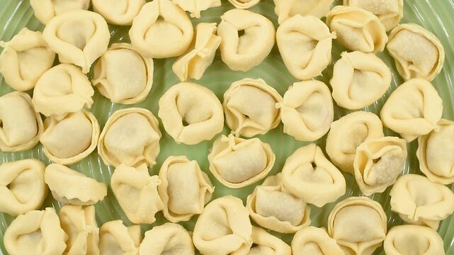 fresh uncooked tortellini filled with prosciutto crudo and parmesan cheese, close-up on a green plate, rotating video.