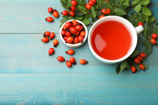 Aromatic rosehip tea in cup, berries and green leaves on light blue wooden table, flat lay. Space for text