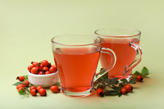Rosehip tea in cups and berries with leaves on light green background