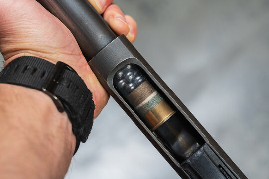 Close up of a man loading a transparent buckshot shell with lead pellets into the magazine tube of a pump action shotgun