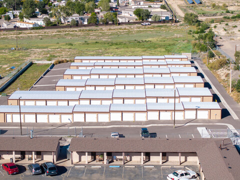 Aerial view of a self-storage facility with rows of metal-roofed units, paved access lanes, and a parking lot in front in Pueblo, Colorado, United States.