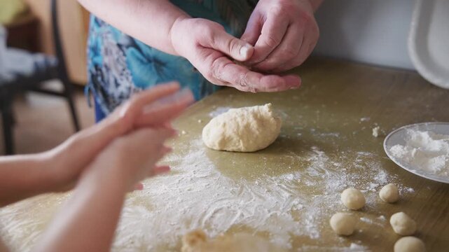 Warm hands knead dough on floured table. Child watches, reaches for dough with curiosity. Mother guides child with gentle, patient touch. Cozy kitchen scene shows bonding through baking